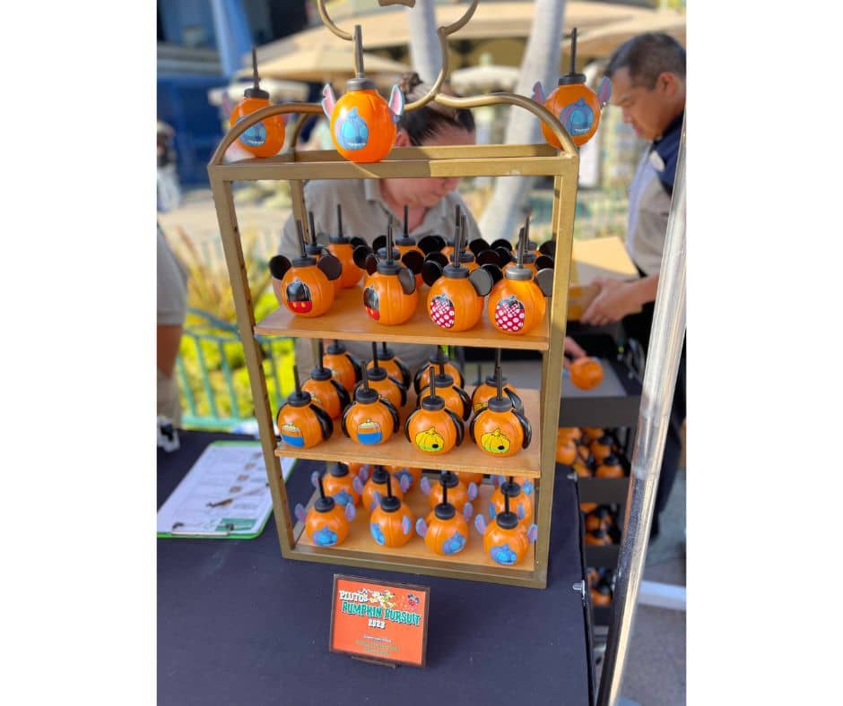 Shelf displaying souvenir pumpkin mini candy buckets featuring Disney characters as prizes for Pluto's Pumpkin Pursuit 2023 in Downtown Disney.