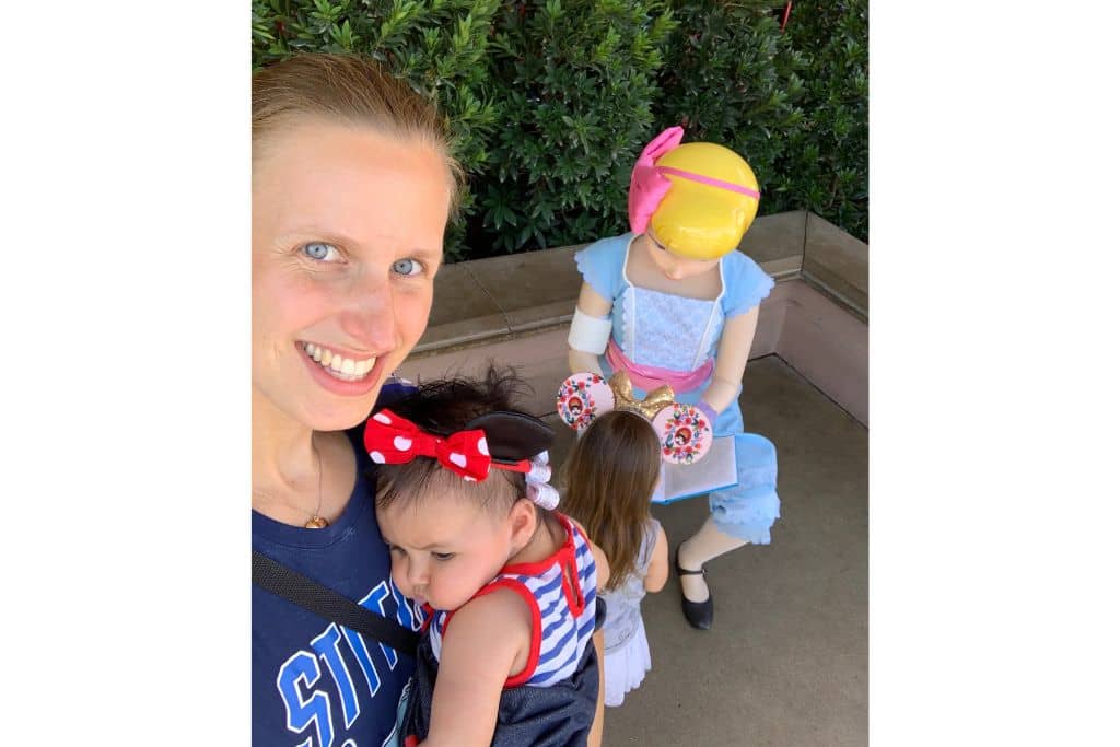 Selfie of Mom holding baby girl while toddler girl gets autograph from Bo Peep at Pixar Pier