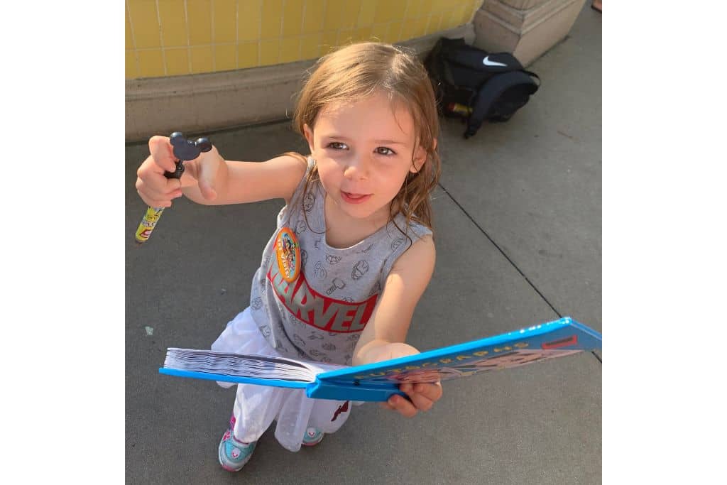 Toddler girld holding up pen and Disneyland Autograph Book