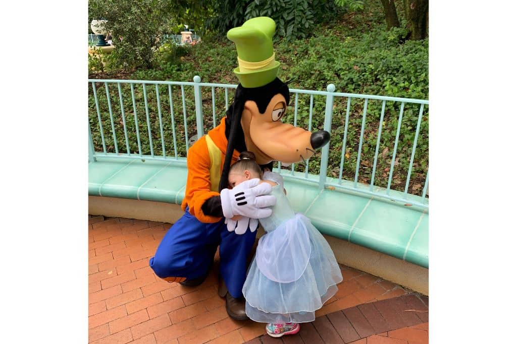 Toddler girl wearing Cinderella dress hugging Goofy at Disneyland