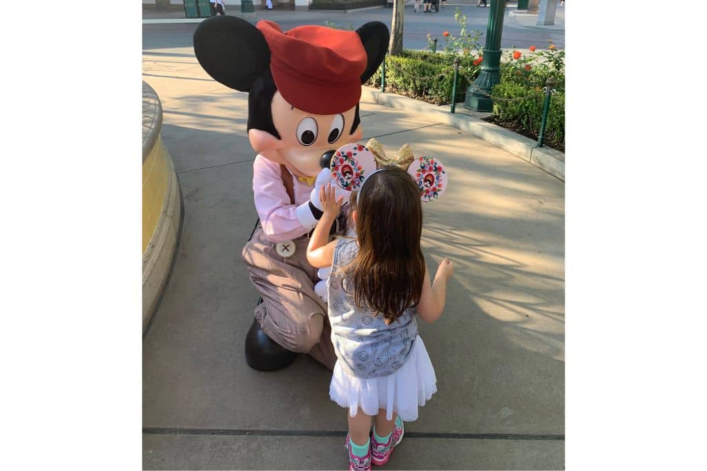 Toddler girl Meeting Mickey Mouse, giving him a high five