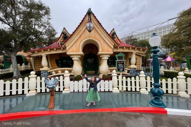 little girl in Anna dress with arms up in front of Mickey Mouse's House in ToonTown at Disneyland.
