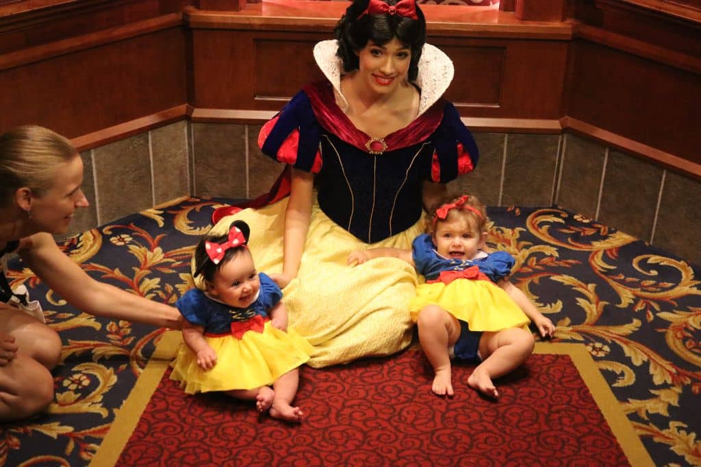 Two baby girls dressed as snowwhite sitting on each side of Snow White at Royal Hall in Disneyland