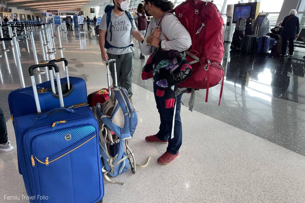 Friends at airport standing next to their luggage. Female friend wearing red backpacking backpack.