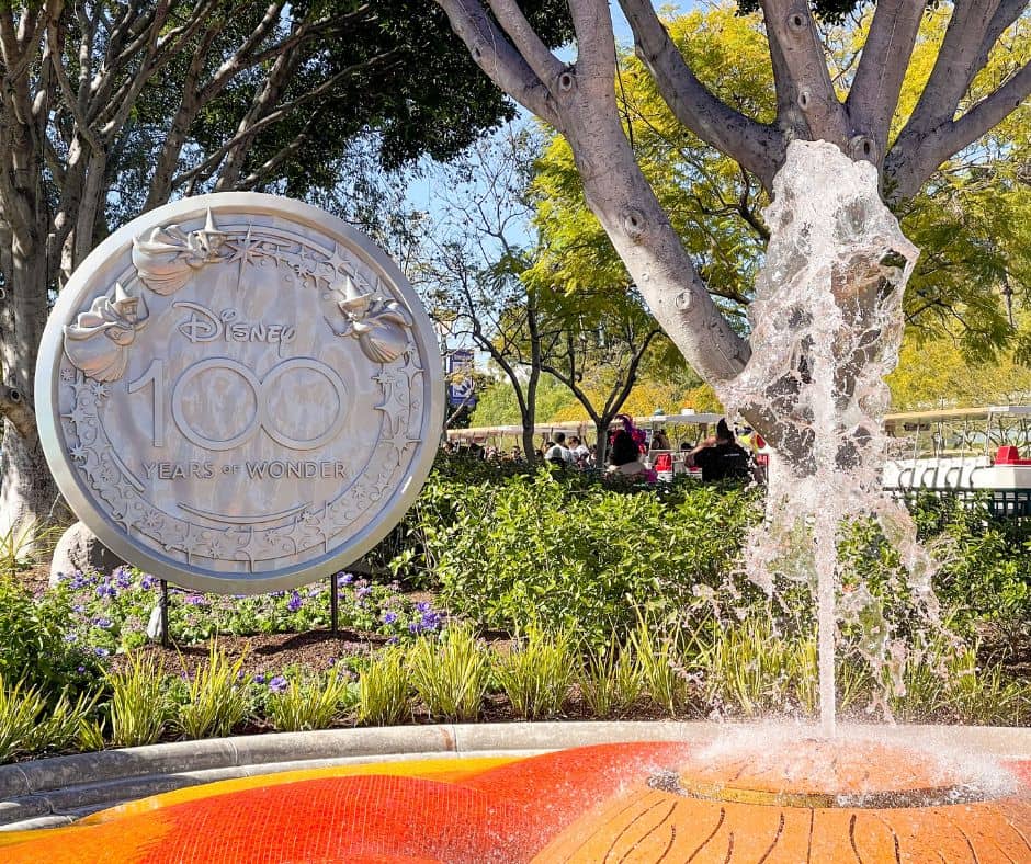 Downtown Disney fountain with silver Disney 100 circular sign behind it.