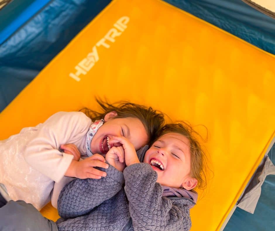 Top half of HeyTrip orange camping mattress with 2 little girls laughing while laying on the mattress.