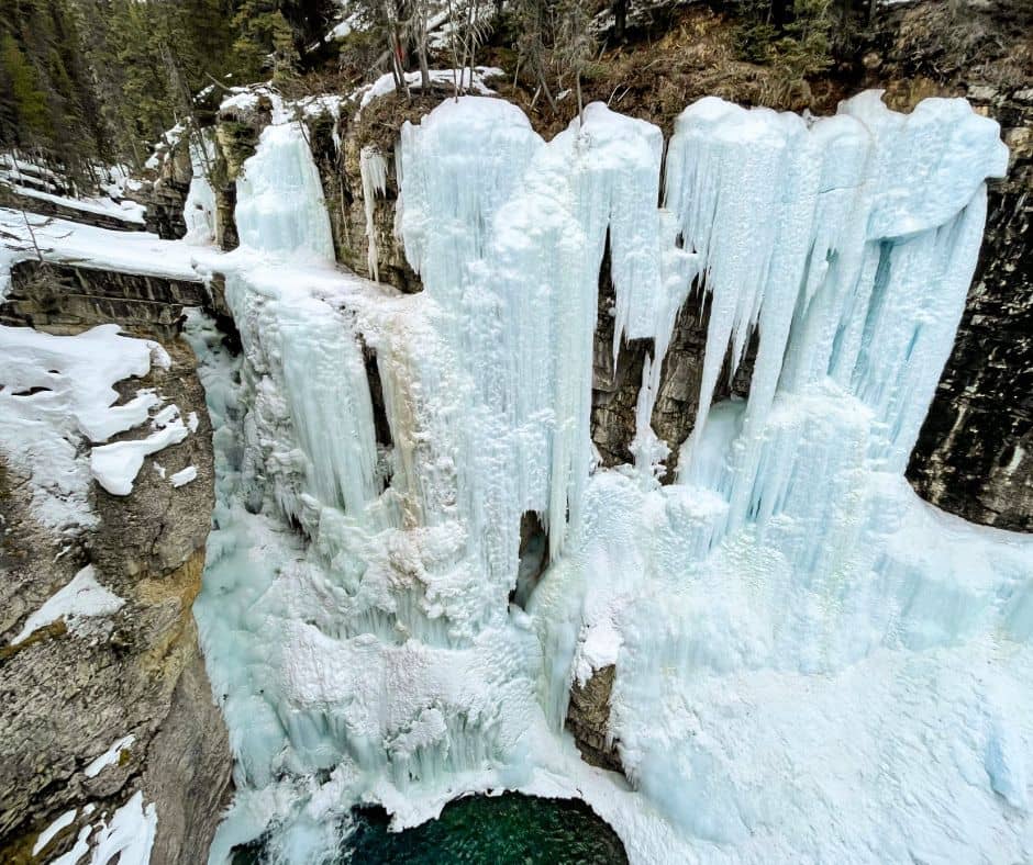 Frozen waterfall cascading down to deep blue pool of water.