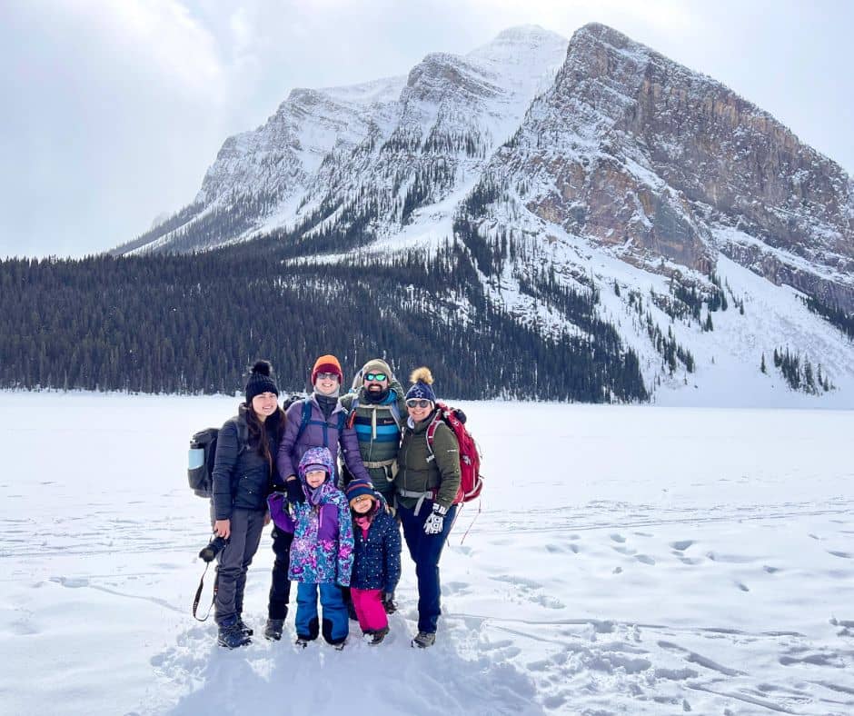 Lake Louise Lakefront Trail group picture of 4 adults and 2 kids on frozen, snow-covered Lake Louise with snow dusted mountain in background.