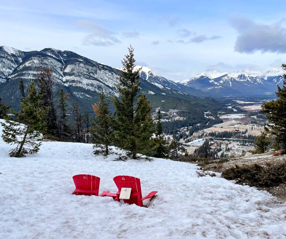Red chairs surrounded by snow at Tunnel Mountain Summit looking over a beautiful valley view
