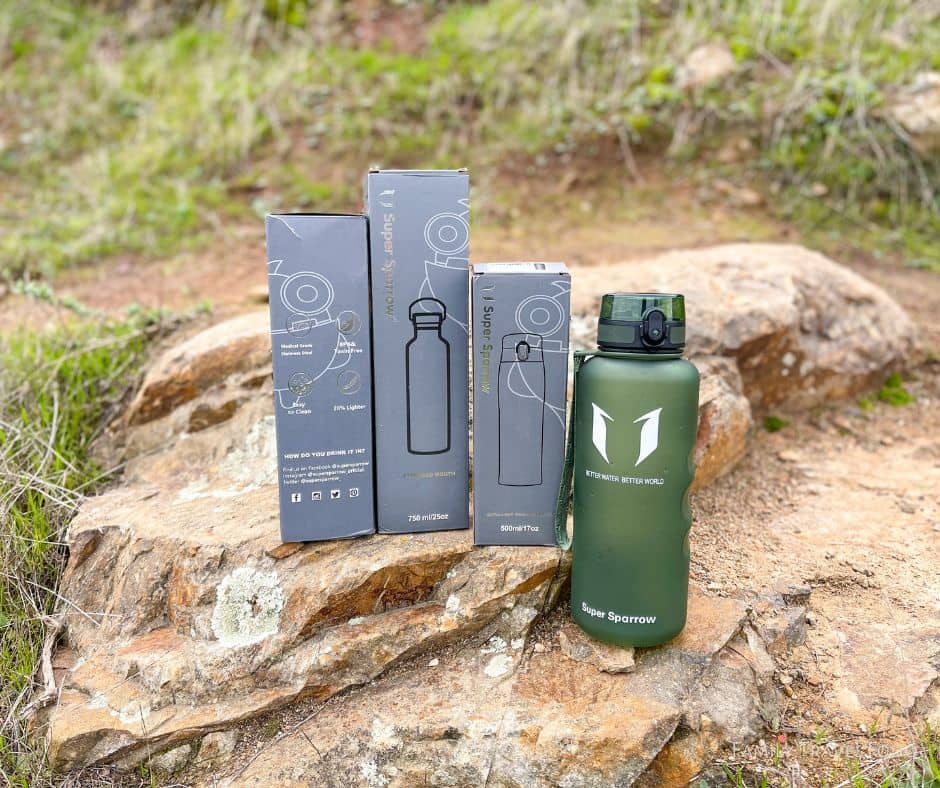 Super sparrow green Tritan water bottle with 3 tall gray super sparrow eater bottle boxes in a row on a rock.