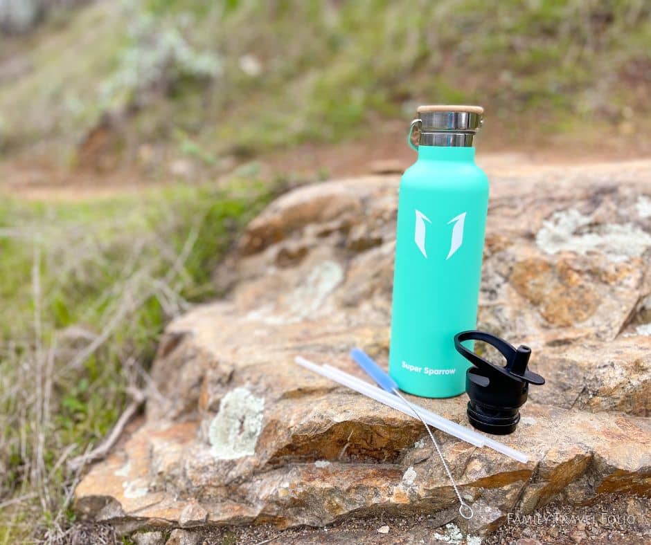 Emerald To Go Series Super Sparrow water bottle with second straw lid, straw, and straw cleaner brush on a rock.