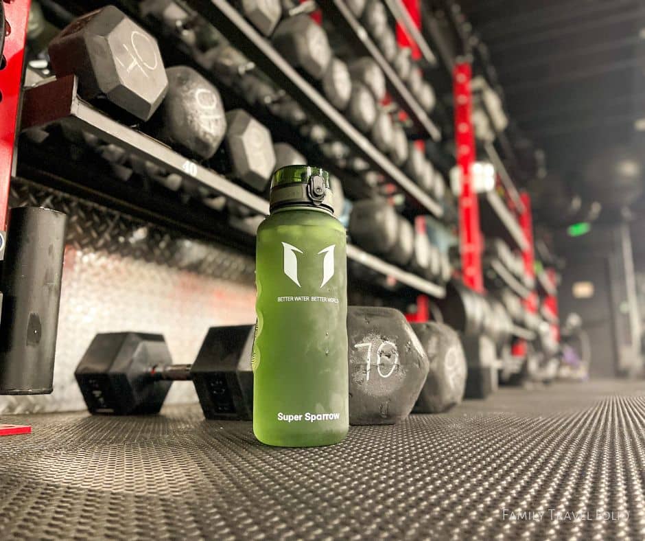 Green Tritan water bottle on the gym floor with weights behind it.