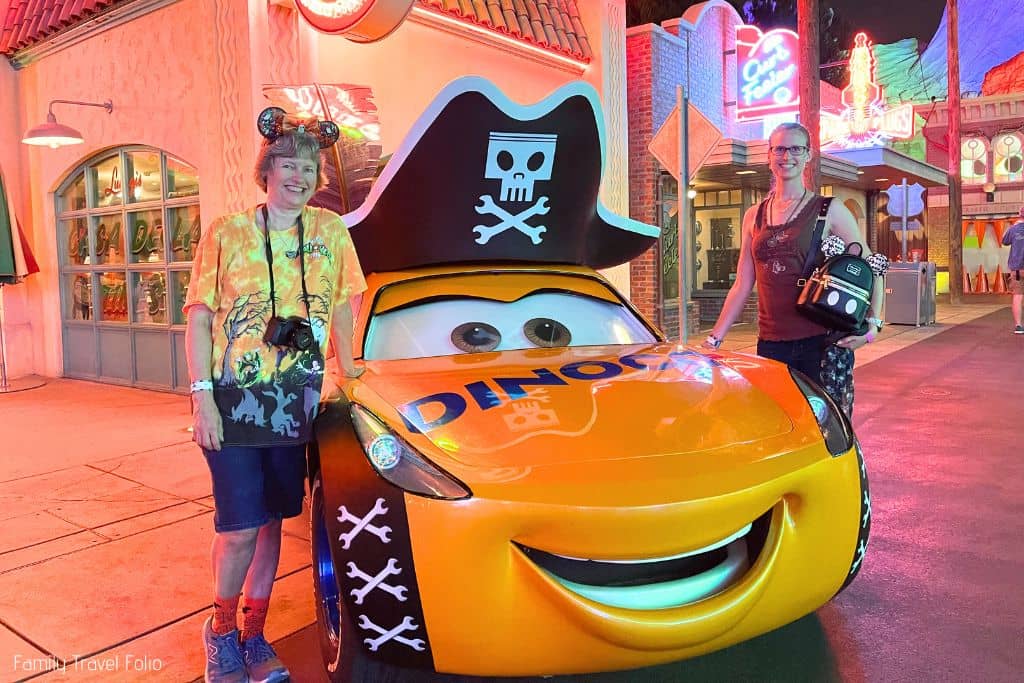 Woman and her mother posing for photo by a yellow Dinoco car with pirate hat.