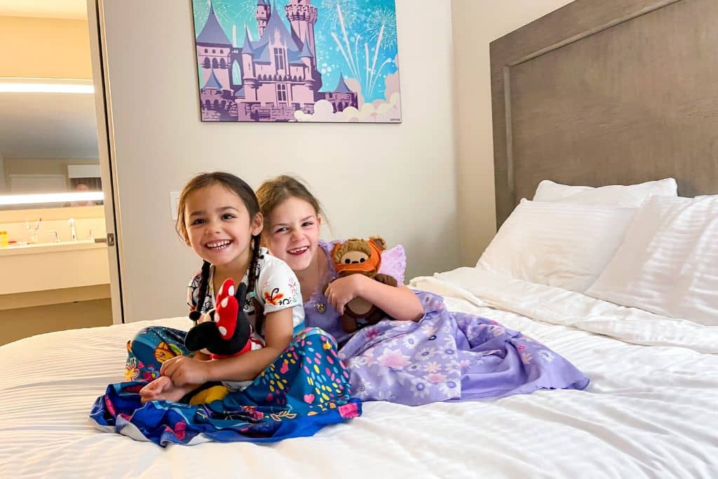 two girls dressed as Isabella and Mirabel sitting on the bed at the Grand Legacy Hotel.