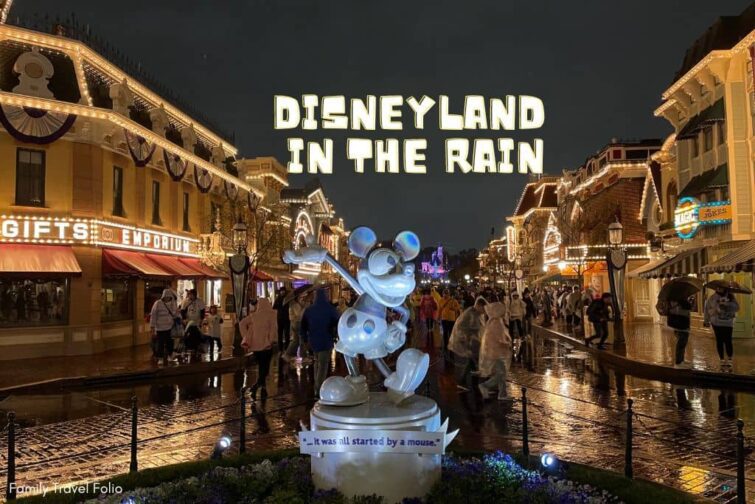 Mickey 100 silver statue with a very wet Main Street USA in the background, lit up with white lights at night on a rainy day at Disneyland.