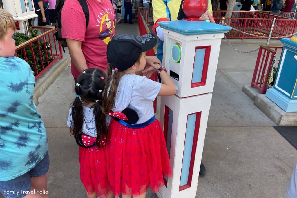 Little girls in Minnie Mouse dresses scanning Magic Band Plus for Genie Plus Lightning Lane