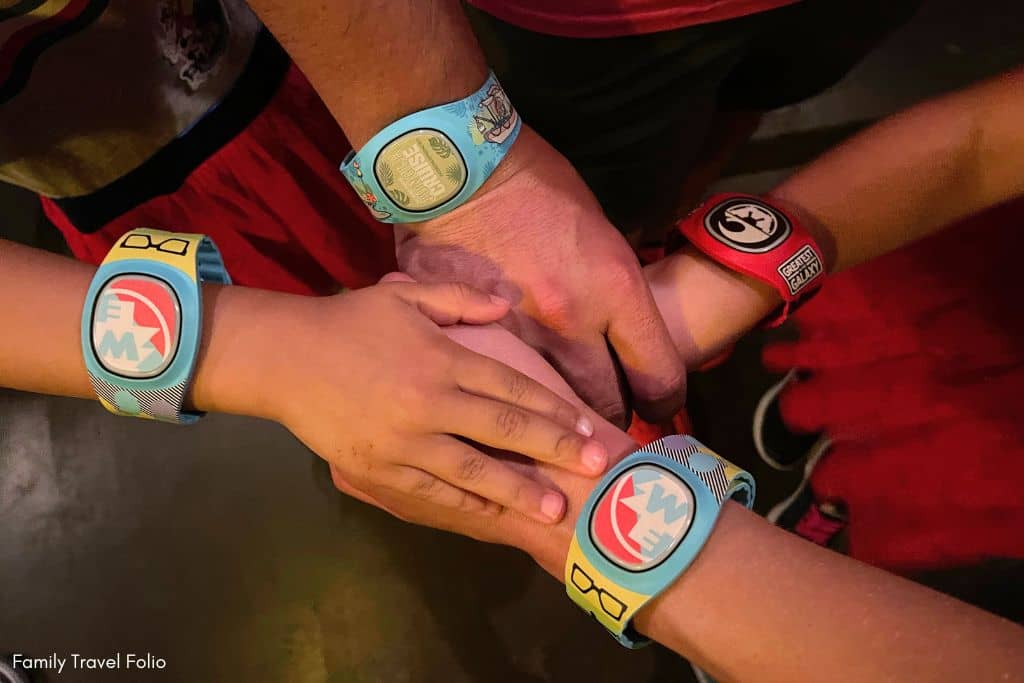 Photo of MagicBand+ on wrists of Mom, Dad, and 2 little girls. They are themed Up, Star Wars, and Jungle Cruise.