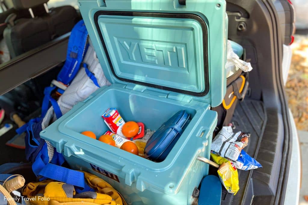 Open cooler filled with healthy road trip snacks for kids including oranges and milk boxes, ensuring nutritious options on the go.