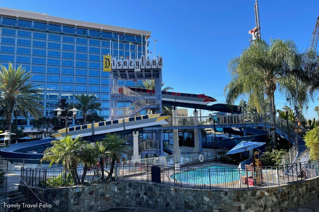 Exterior view of the Disneyland Hotel showcasing the iconic monorail waterslide and lush palm trees.