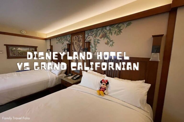 Image of the Grand Californian Hotel beds with tree decal on wall. The words "Disneyland Hotel vs Grand Californian are in the middle of the picture in white block letters with dark brown outline.