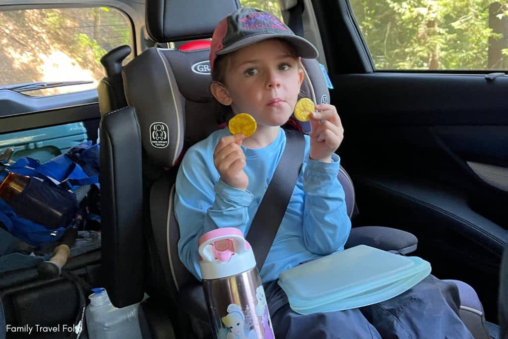 Young child holding up two fried plantain chips, a tasty and crunchy alternative to traditional road trip snacks for kids.