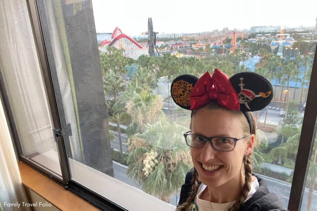 Guest wearing whimsical Mickey Mouse ears with a stunning view of Disney California Adventure Park from a hotel room.