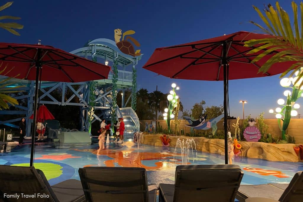 Evening atmosphere at the Pixar Place Hotel pool with a fun splash pad area, illuminated for nighttime enjoyment.