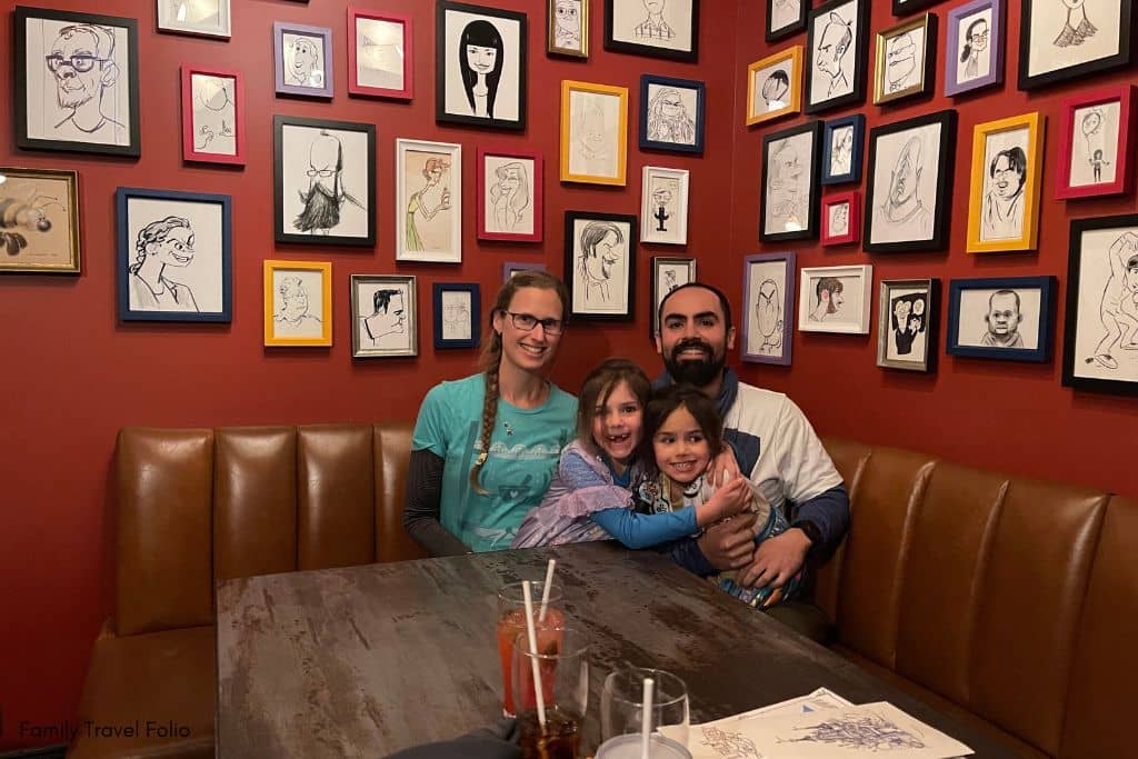 Family enjoying the cozy and art-filled secret room at Lamplight Lounge in Disneyland, perfect for escaping the rain and having a delightful meal together.