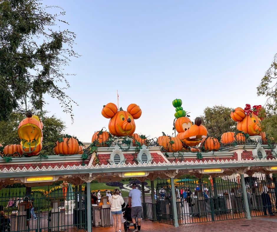 Disneyland entrance decorated with large pumpkin sculptures shaped like Mickey, Goofy, and Minnie, welcoming visitors during Halloween time in October.