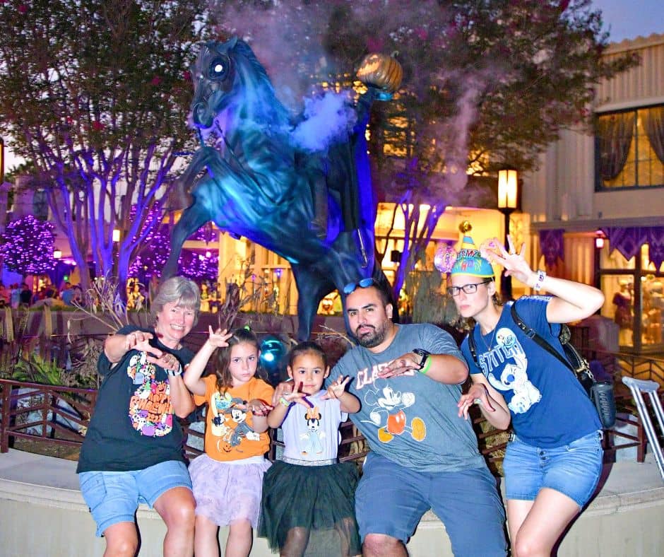 Family posing with playful spooky expressions in front of the Headless Horseman statue during Oogie Boogie Bash at Disney California Adventure.