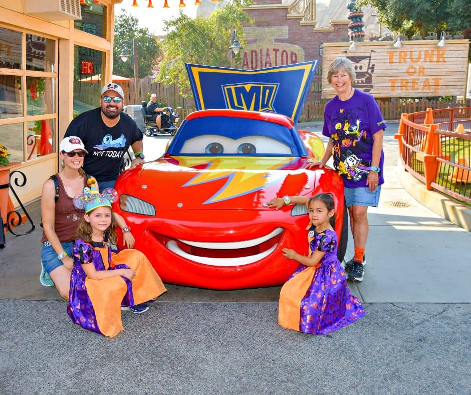 Family posing with Lightning McQueen dressed in a Halloween-themed paint job at Cars Land, Radiator Springs, during Disneyland’s Halloween celebration.