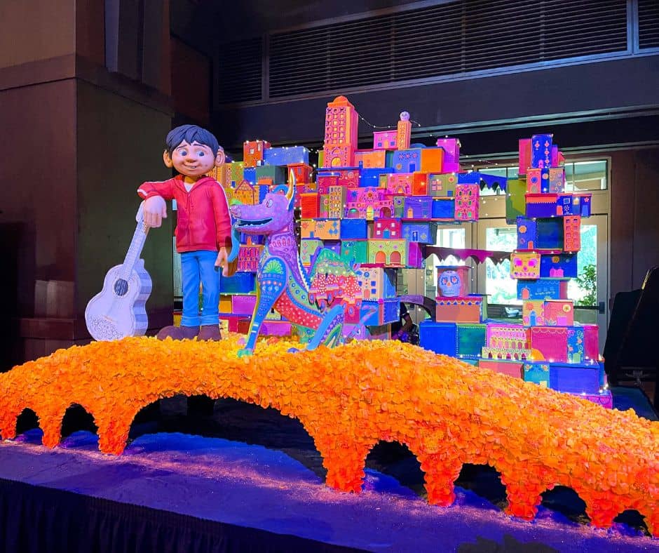 Colorful Day of the Dead display at Disney's Grand Californian Hotel featuring Miguel and Dante from the movie 'Coco,' with vibrant marigold flowers and decorations during Disneyland's October celebration.