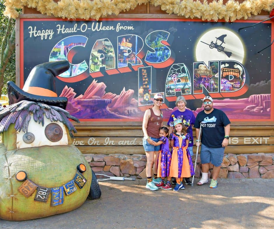 Family dressed in Halloween themed outfits at Cars Land in Disneyland, standing by the "Happy Haul-O-Ween" sign, enjoying the festive atmosphere despite the hot October weather.