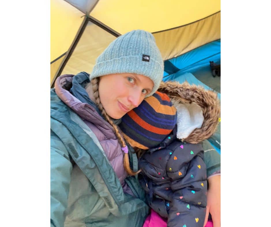 Mom cuddling her child inside a tent, both dressed in cozy winter clothing to stay warm.