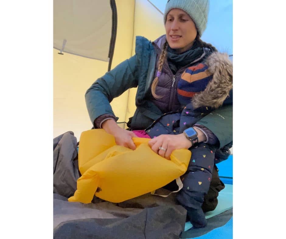 Mom inflating a camping mattress inside a tent as part of staying comfortable and warm during cold camping.