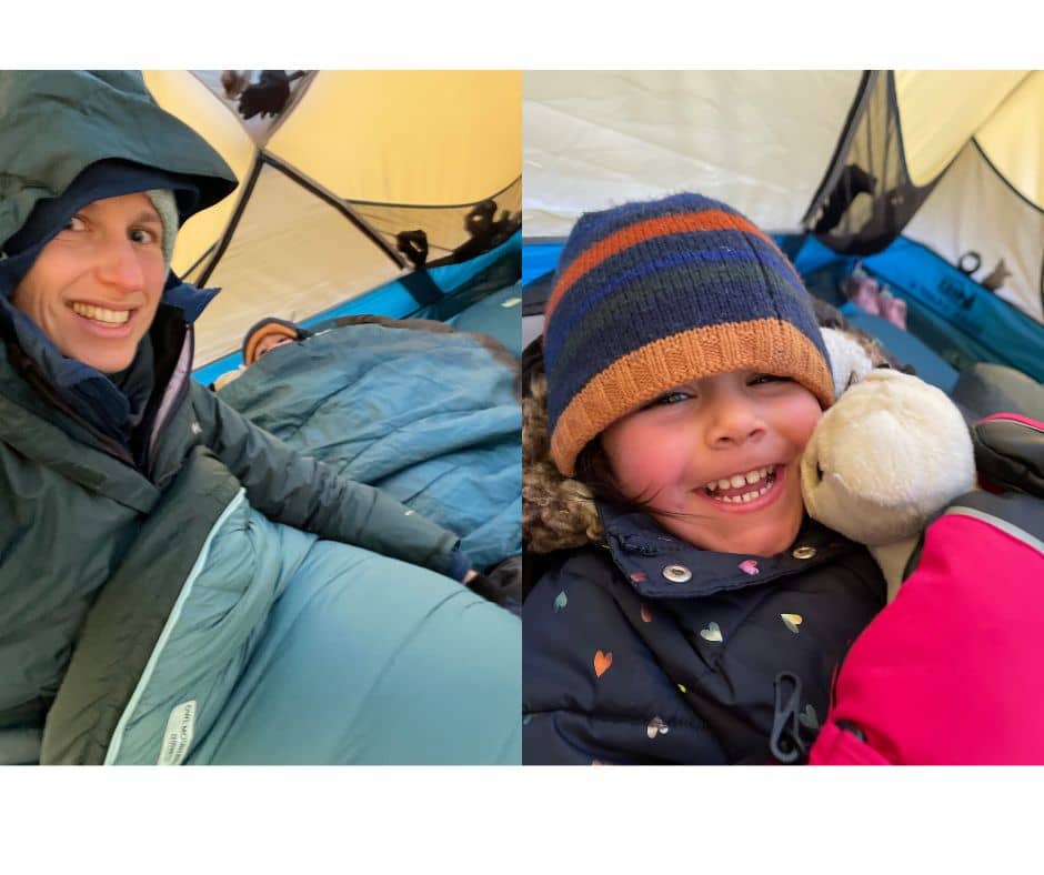 Mom smiling in her sleeping bag and a child cuddling a plush toy, both cozy and warm inside a winter camping tent.