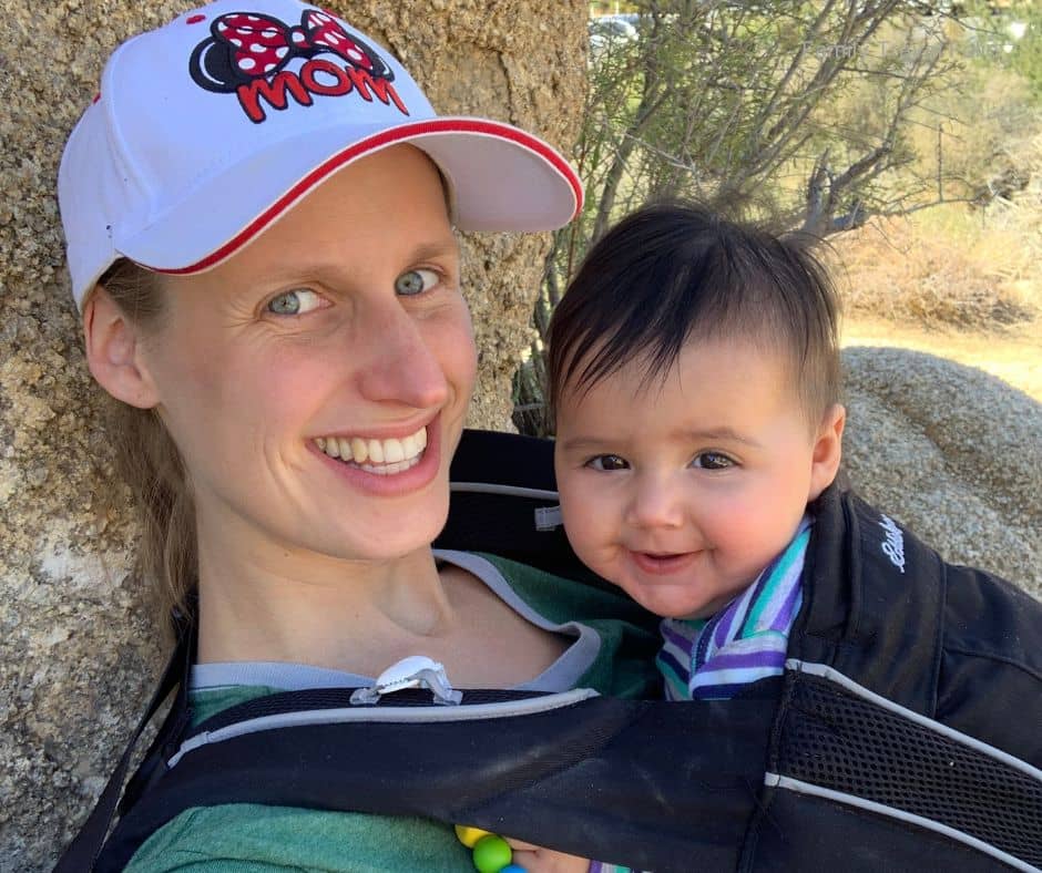 Mom smiling while baby is carried in a front carrier on a family-friendly hiking trail