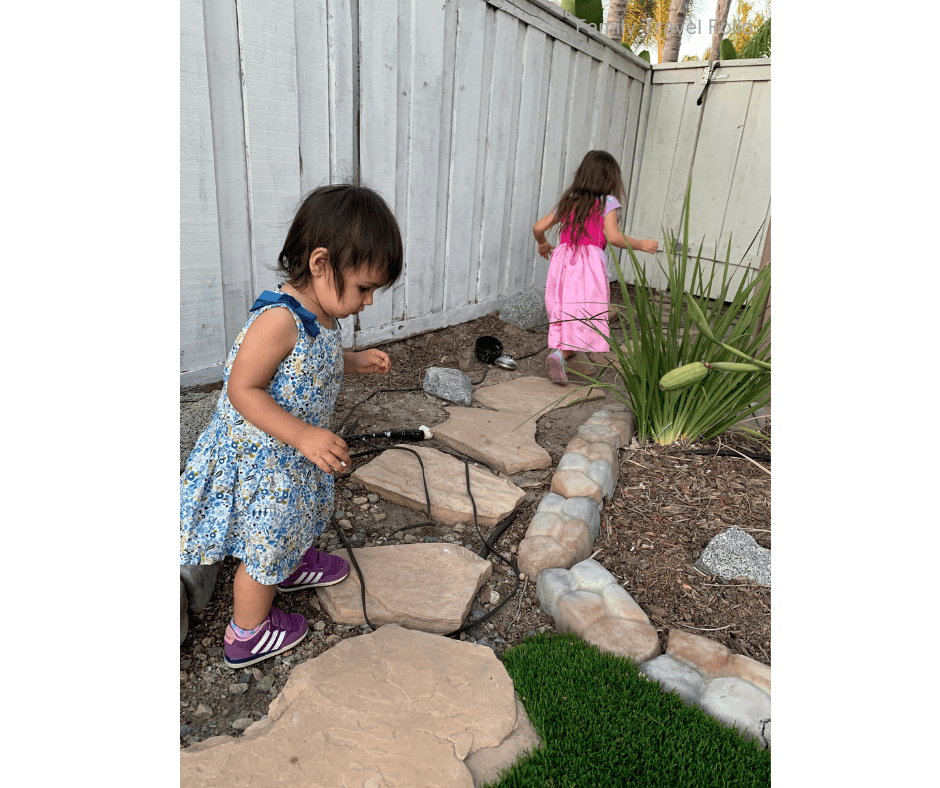 Two young girls exploring a garden path in a backyard with stepping stones and plants