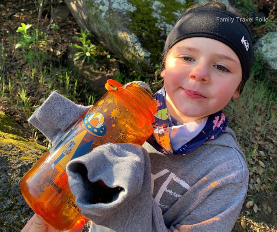 Young child holding a water bottle during a hike, staying hydrated on the trail