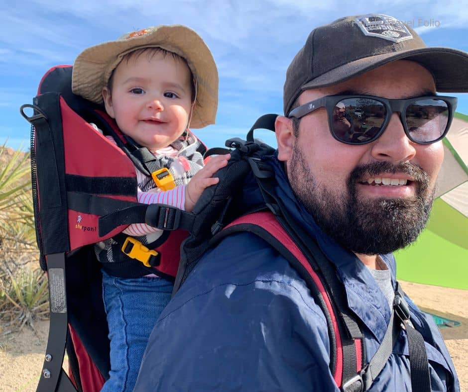 Smiling baby in a framed hiking carrier on dad’s back during a sunny desert hike