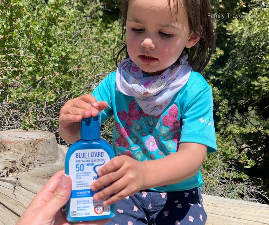 Toddler applying Blue Lizard sunscreen while hiking on a sunny day in the forest