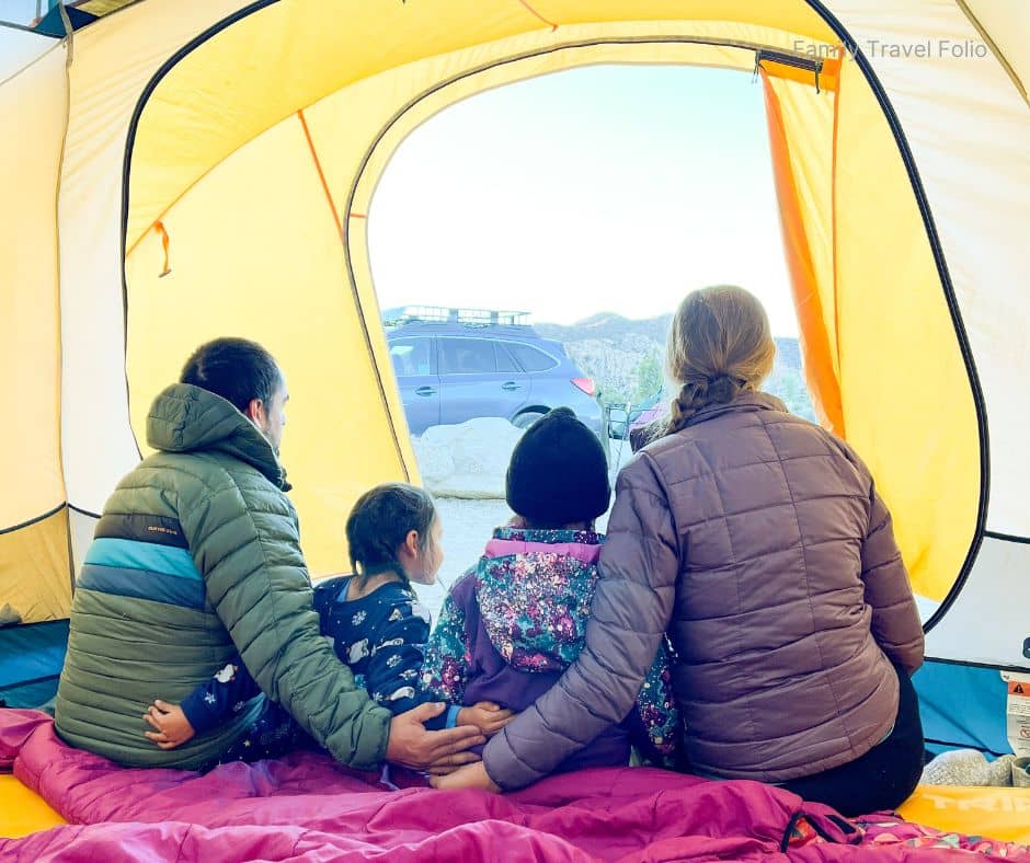 Family sitting inside tent looking out at parked car – Budget-friendly family vacation camping experience.