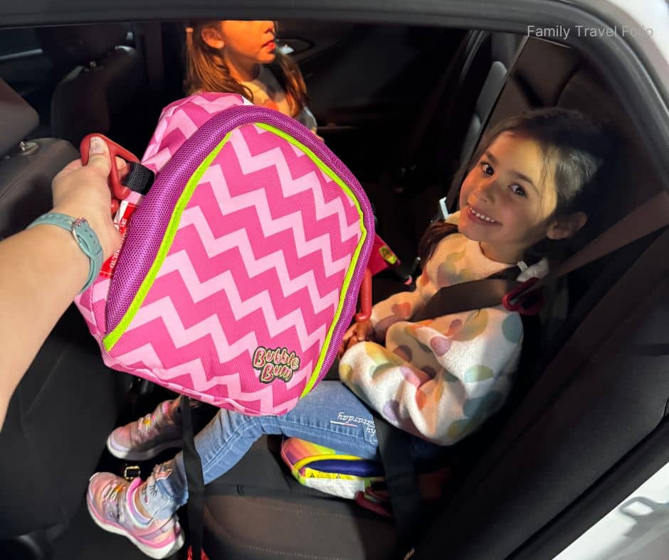 Child in backseat with portable booster seat – Budget-friendly family travel tip for safe, compact car seat solution.