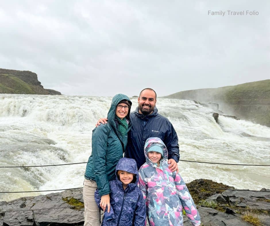 Family wearing rain jackets posing in front of Gullfoss waterfall on a cloudy day, capturing one of the most iconic things to do in Reykjavik and the Golden Circle.