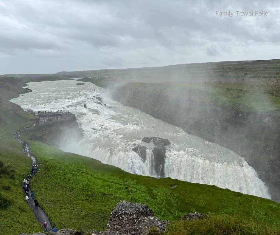Wide view of Gullfoss waterfall cascading through a misty canyon surrounded by green hills, one of the most breathtaking natural things to do in Reykjavik along the Golden Circle.