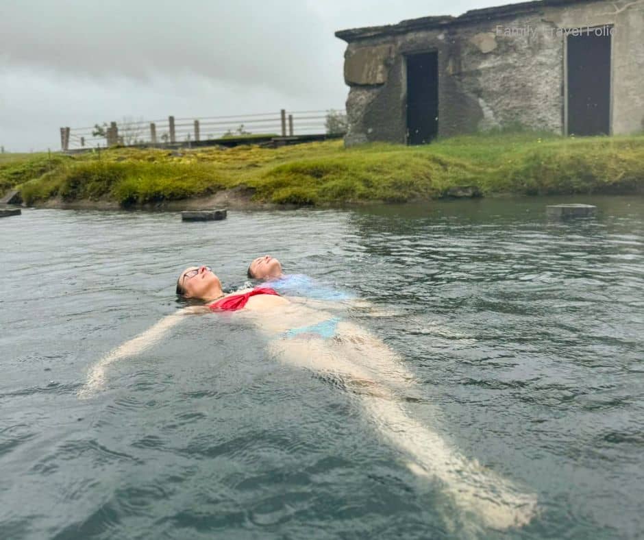 Two people floating peacefully in a natural hot spring surrounded by mossy rocks and misty air, highlighting one of the most relaxing things to do in Reykjavik for travelers seeking geothermal experiences.