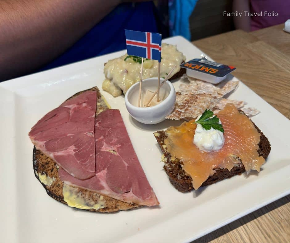 Traditional Icelandic tasting plate with smoked lamb, salmon on rye bread, fish stew, and crispbread topped with an Icelandic flag — a must-try food experience and one of the cultural things to do in Reykjavik.