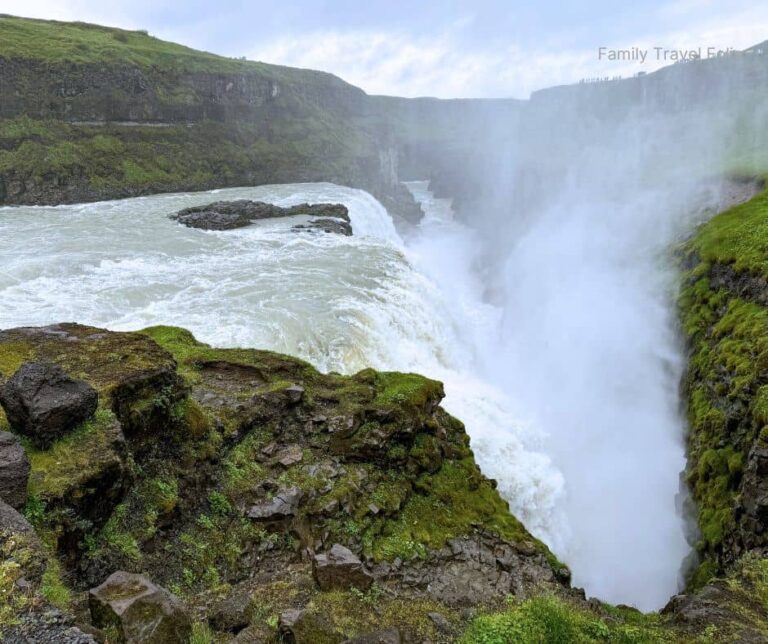 Powerful waterfall surrounded by green cliffs and mist rising into the cloudy Icelandic sky, capturing the raw beauty of Gullfoss — one of the top outdoor things to do in Reykjavik and the Golden Circle area.