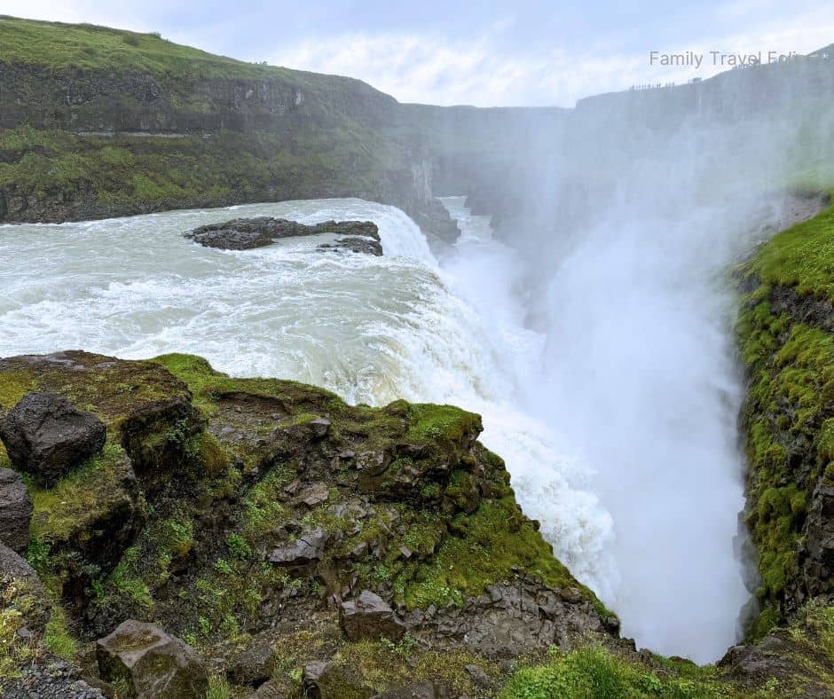 Powerful waterfall surrounded by green cliffs and mist rising into the cloudy Icelandic sky, capturing the raw beauty of Gullfoss — one of the top outdoor things to do in Reykjavik and the Golden Circle area.