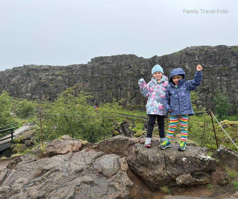 Two kids in colorful rain jackets standing on a rocky overlook in Thingvellir National Park, a UNESCO World Heritage Site and one of the most educational and scenic things to do in Reykjavik with kids.